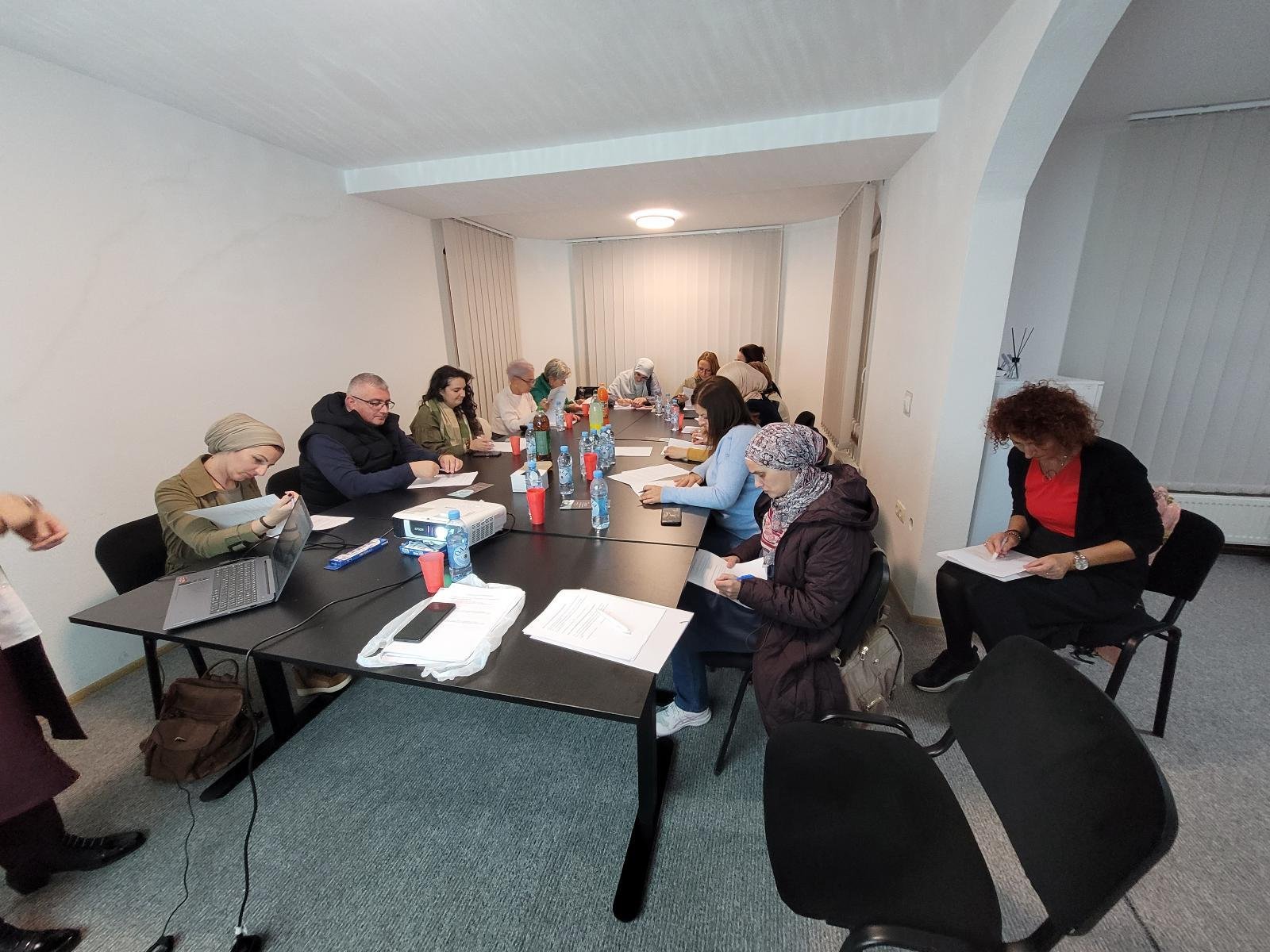 Učesnici radionice za stolom, projektor u prostoriji